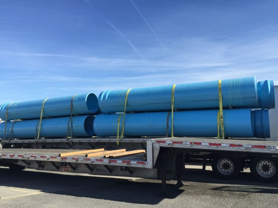 flatbed trailer with large blue plastic pipes loaded and strapped to it
