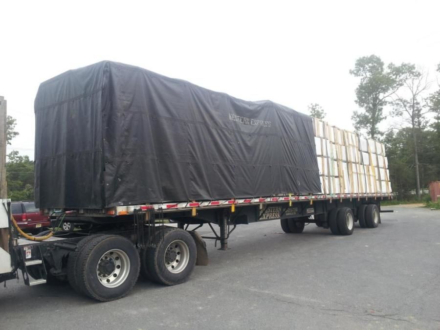 flatbed trailer loaded with bundles of vinyl tarped and strapped