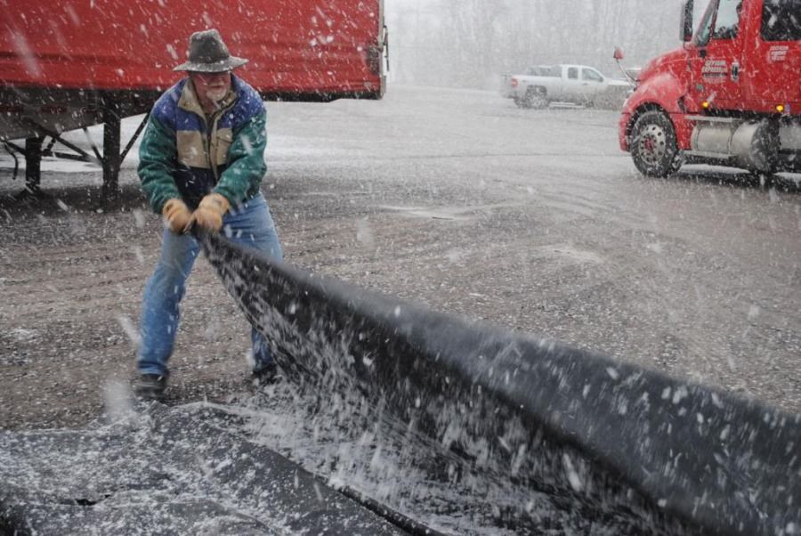 flatbed truck driver folding up his tarp in the winter
