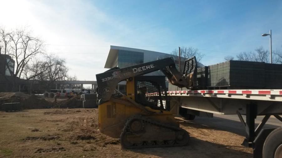 Bobcat unloading a flatbed truck on a gravel lot at a construction site.