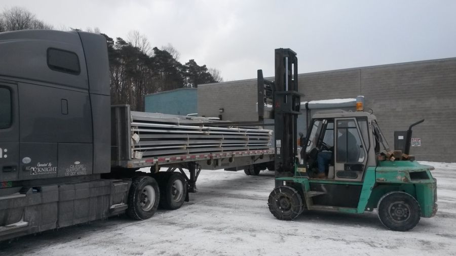 forklift with chains on tires unloading flatbed trailer after snow and ice storm
