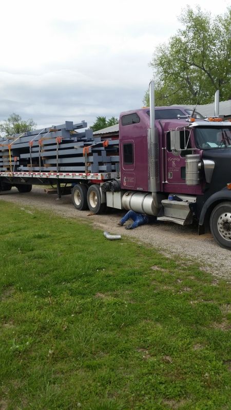 purple flatbed trailer loaded with metal beams in trucking school with trainer fixing exhaust leak