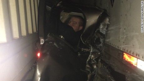 car crushed between two tractor trailers with survivor looking out