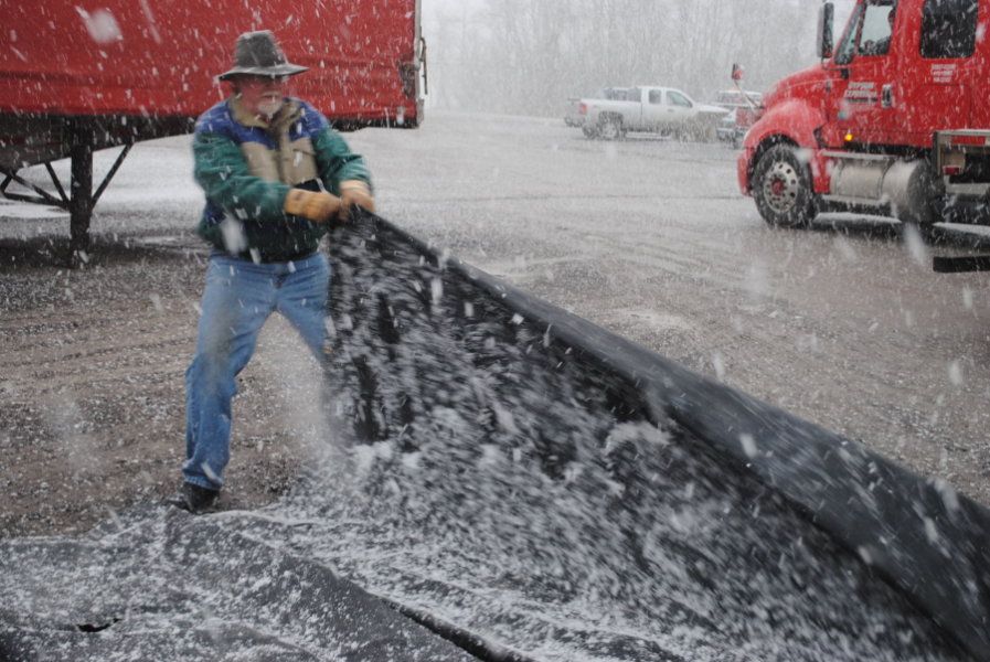 old bearded truck driver tarping a flatbed in the snow