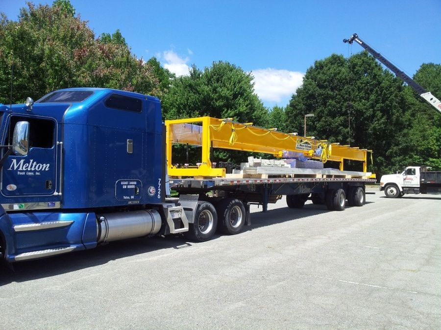 crane loading metal frames on a blue Melton flatbed truck