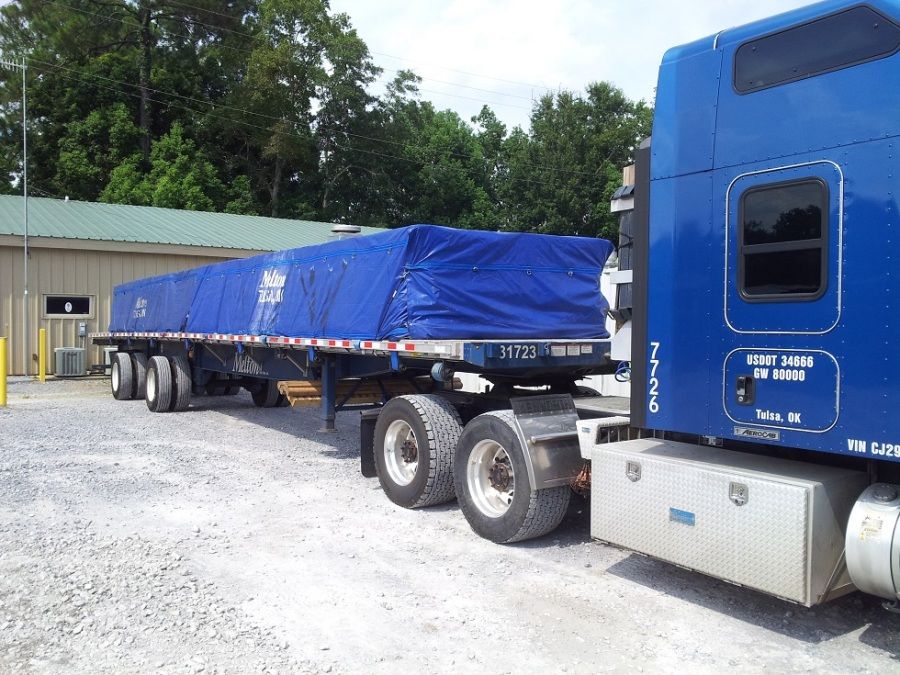 flatbed trailer loaded and tarped with barrels of resin oil for drilling rigs in the oil fields