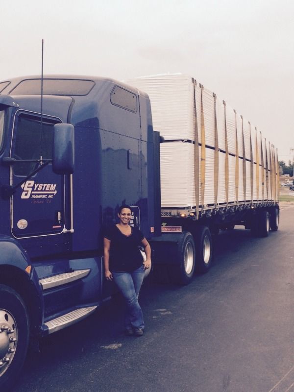 Woman truck driver standing by her blue System Transport flatbed loaded and strapped