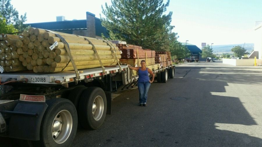 woman truck driver standing next to flatbed trailer loaded with lumber