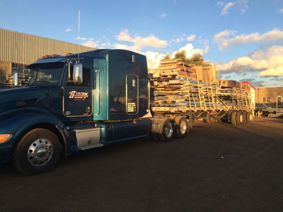 blue System truck pulling flatbed trailer stacked with pallets and strapped