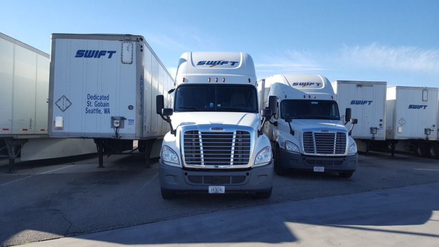 front view of white Swift tractor-trailer semi trucks and trailers parked in the lot
