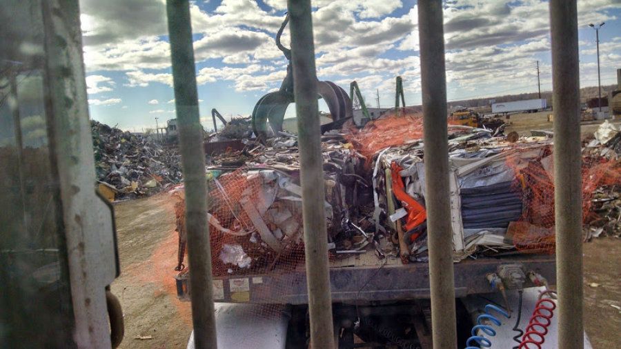 Truck driver's view of scrap metal being unloaded from a flatbed trailer through the rear cab window