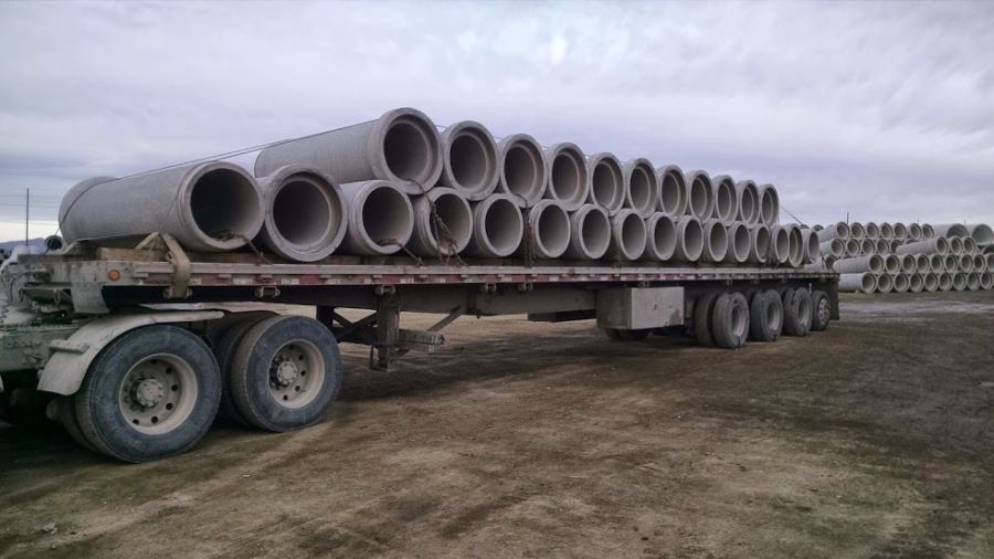 single row of cement bell-end pipe loaded eyes cross-wise and chained on flatbed trailer with empty spaces on top row