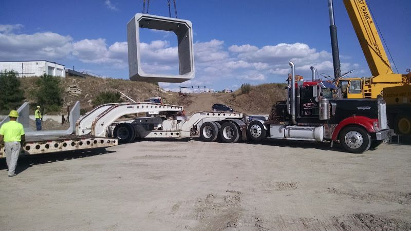 oversize flatbed being loaded with cement boxes by a crane