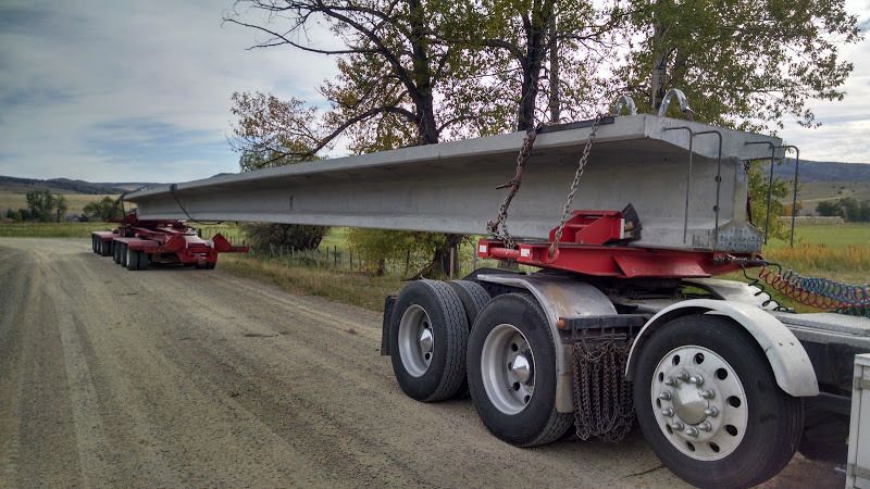 flatbed trailer and dolly loaded with oversized cement bridge beams