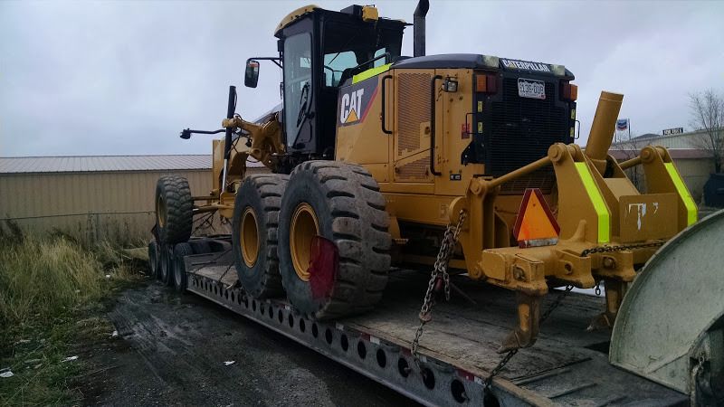 large yellow CAT grader loaded and chained on flatbed trailer